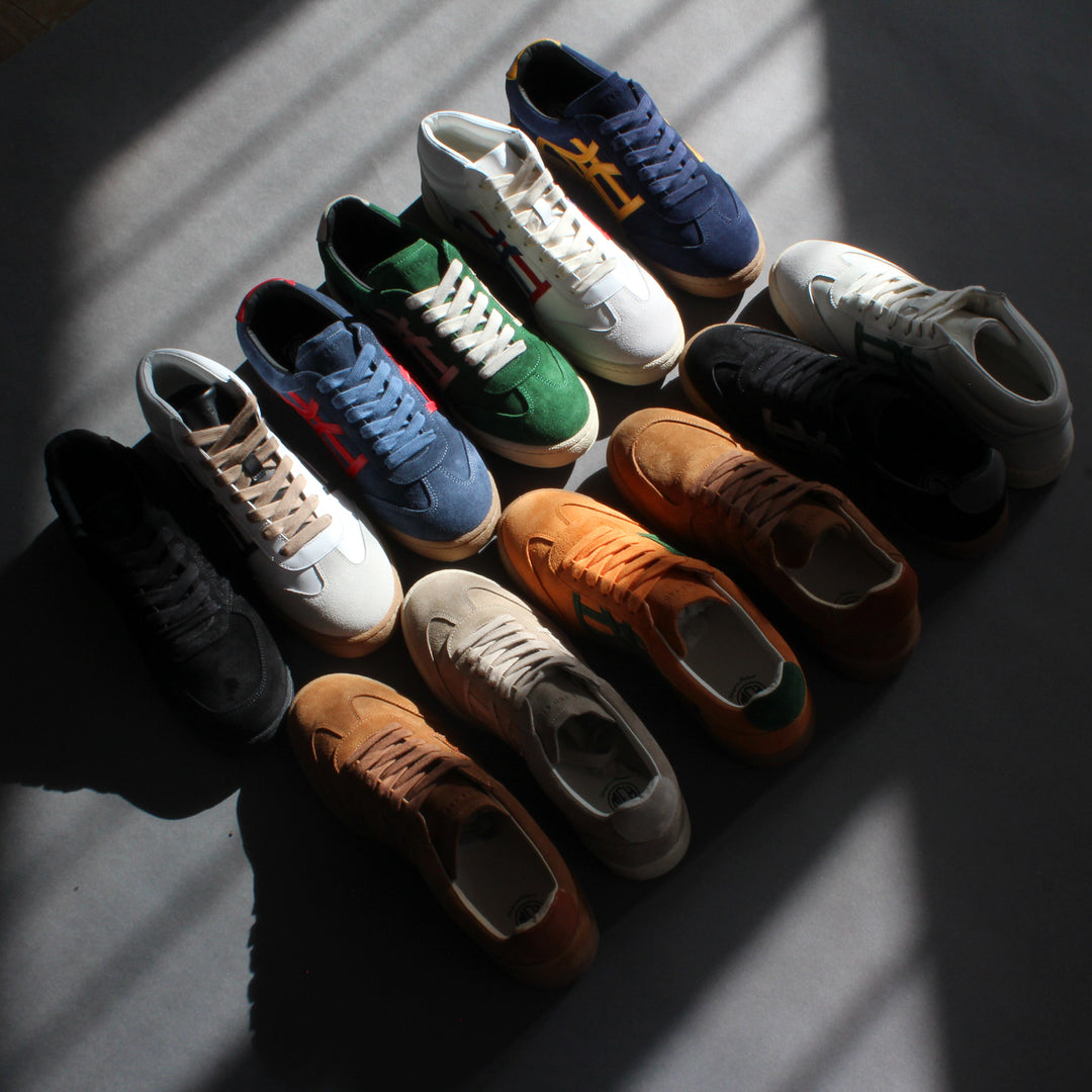 An array of different color sneakers aligned diagonally across the floor. There is light shining on them.
