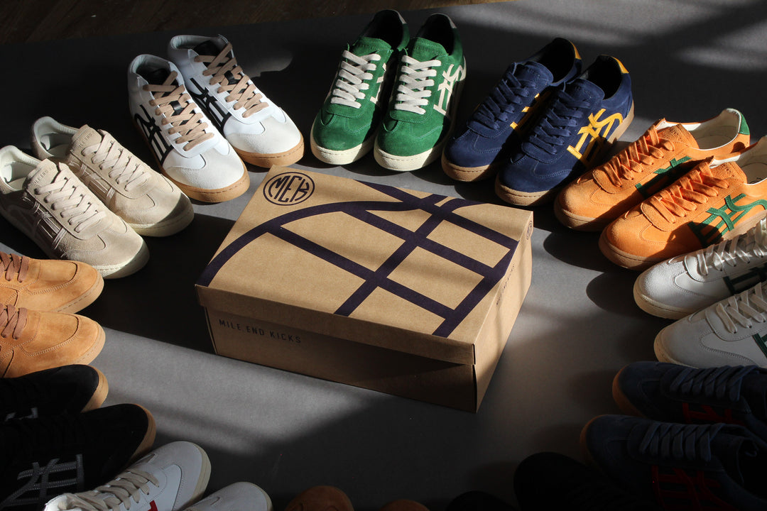 Different high and low top suede and leather sneakers arranged in a circle around a shoe box with black lines on it.