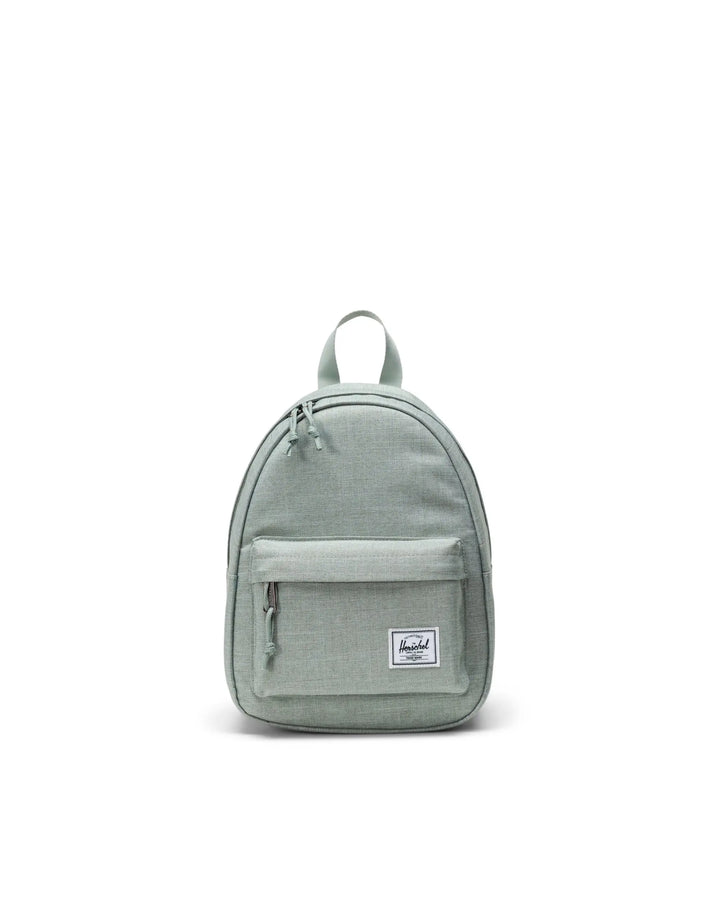 A compact green Herschel Classic Mini Backpack with front pocket and brand label visible.