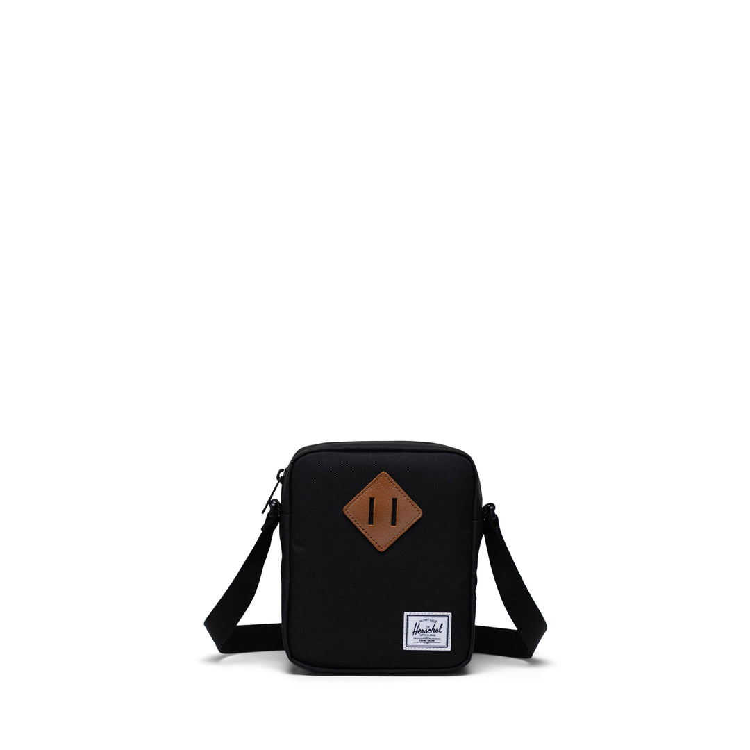 A black Herschel Heritage crossbody bag with an adjustable strap and a signature diamond detail on the front.