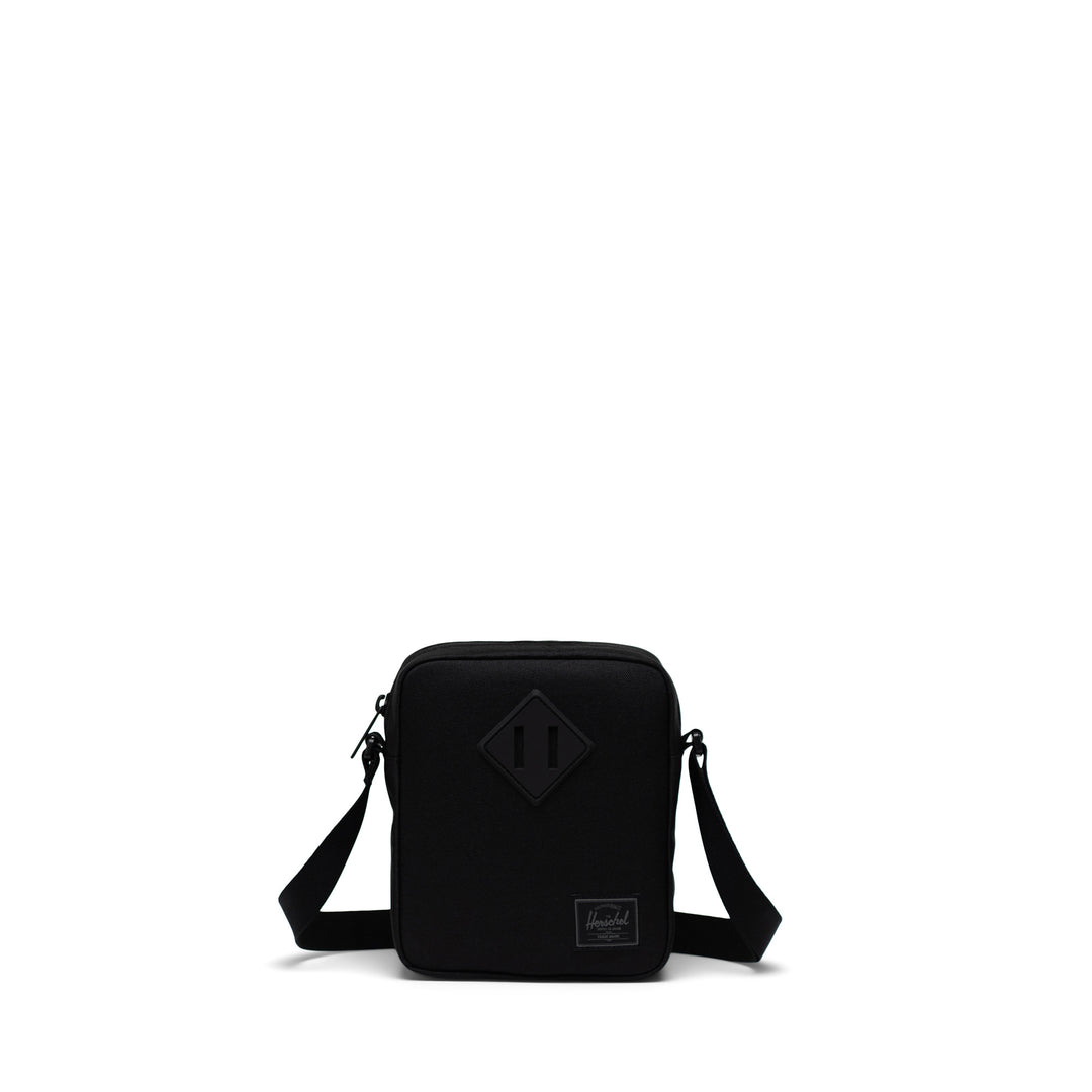 A black Herschel Heritage crossbody bag with an adjustable strap and a signature diamond detail on the front.