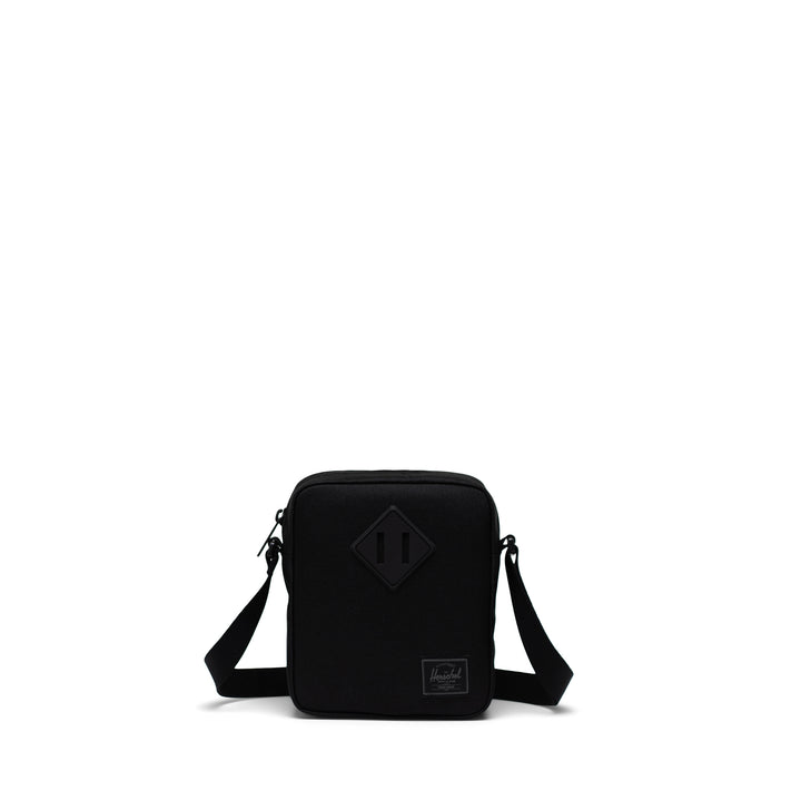 A black Herschel Heritage crossbody bag with an adjustable strap and a signature diamond detail on the front.