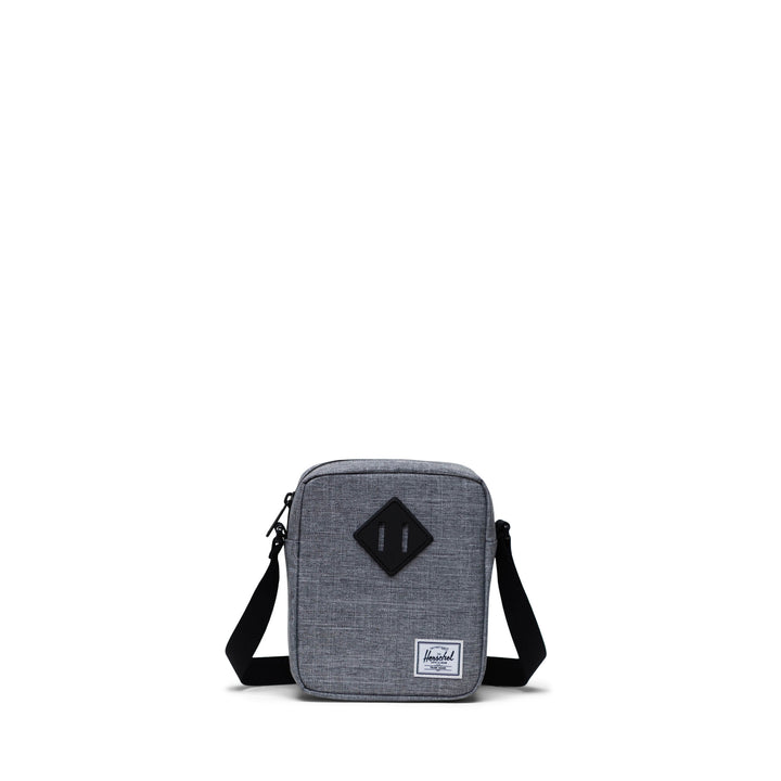 A grey Herschel Heritage crossbody bag with an adjustable strap and a signature diamond detail on the front.