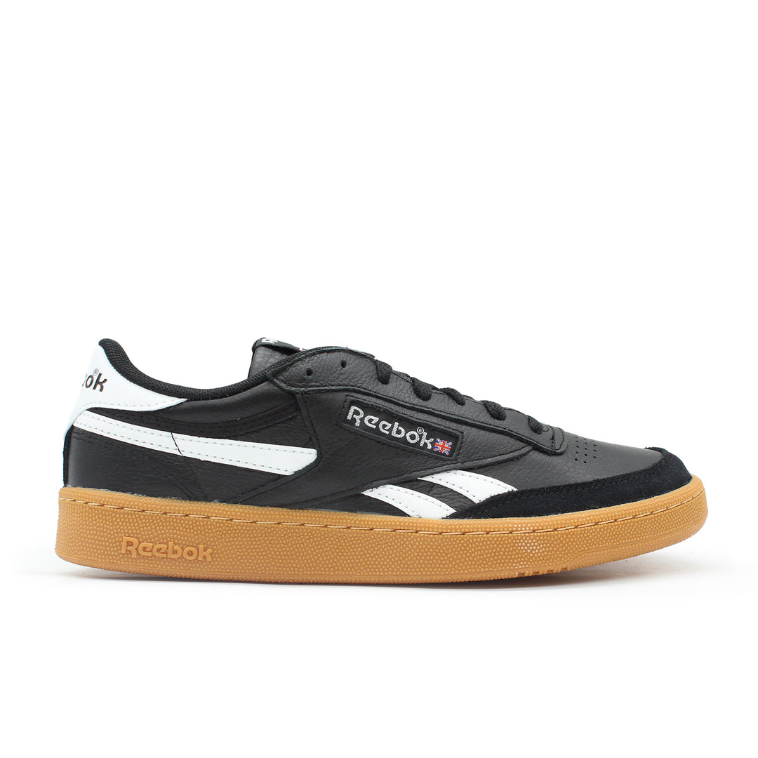 The side view of a black Reebok shoe. The sole is gum colored. There is a union jack flag next to the Reebok logo on the shoe.