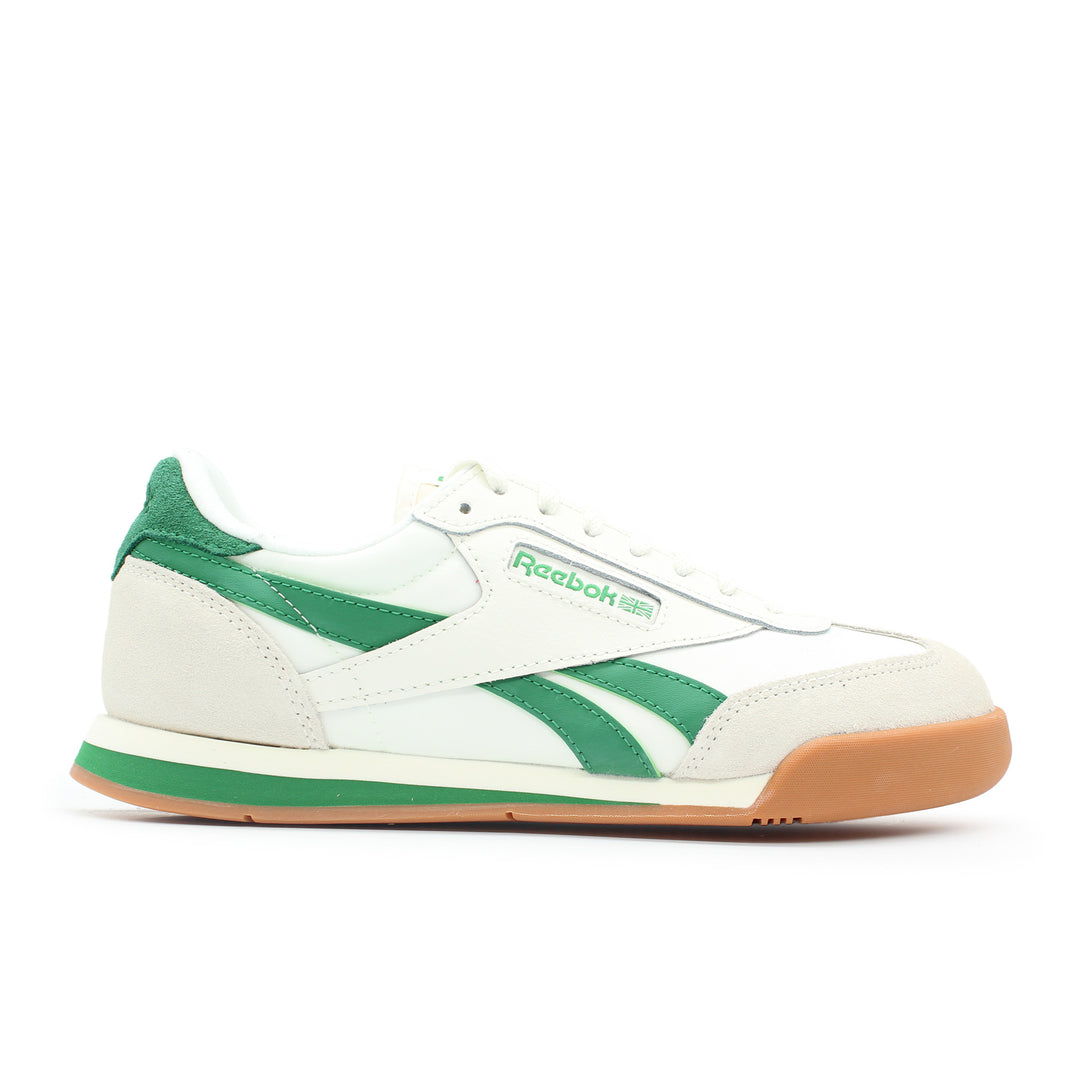 The side view of a white and green Reebok shoe. The sole is gum colored. The shoe is made of leather and suede.