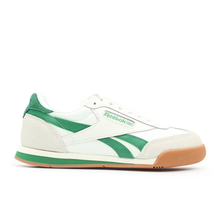 The side view of a white and green Reebok shoe. The sole is gum colored. The shoe is made of leather and suede.