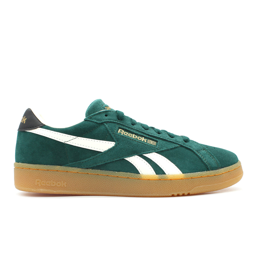 The side view of a dark green suede Reebok shoe on a white background. The shoe has a gum slightly translucent sole and midsole. It has white and gold accents.