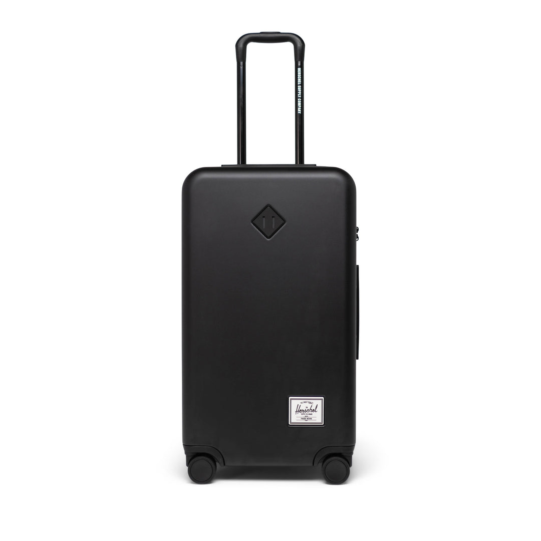 A black Herschel Heritage hardshell luggage with telescopic handle and four wheels.