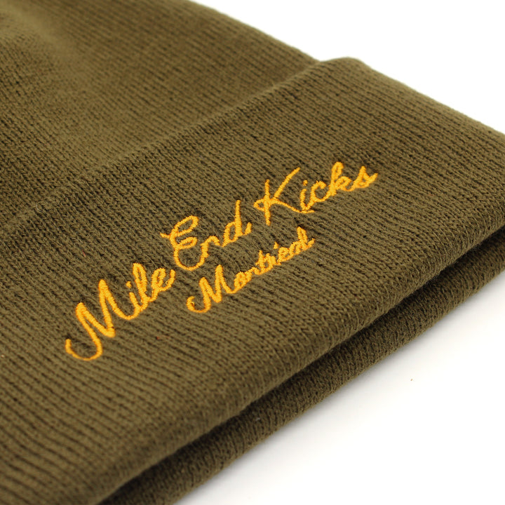Green knit beanie with 'Mile End Kicks Montreal' embroidery on a white background
