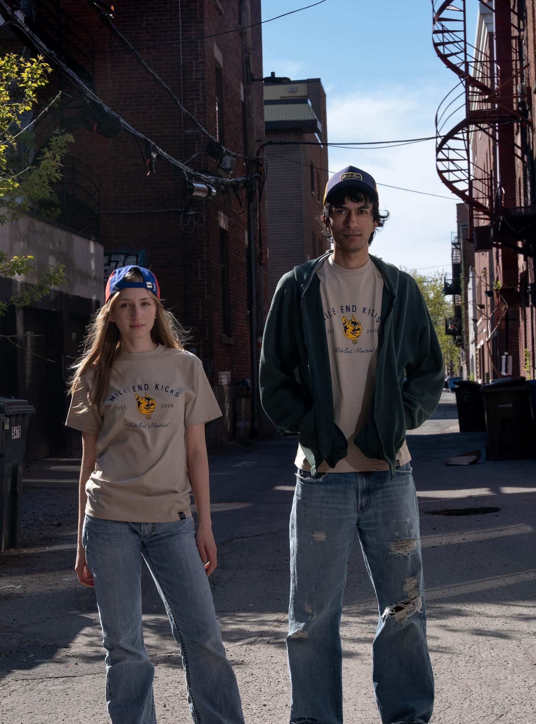 Two people standing on a street with buildings and a clear sky in the background