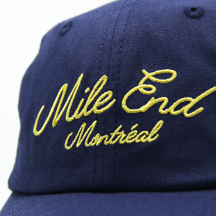 Navy blue cap with yellow embroidered text 'Mile End Montreal' on a white background