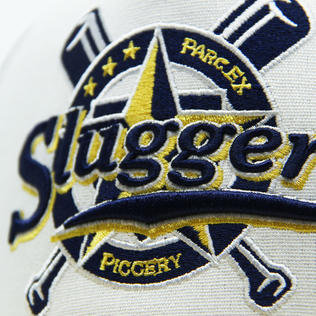 Close-up of a 'Sluggers' logo with crossed bats and 'Parc Ex Piggery' text on hat on a white background.