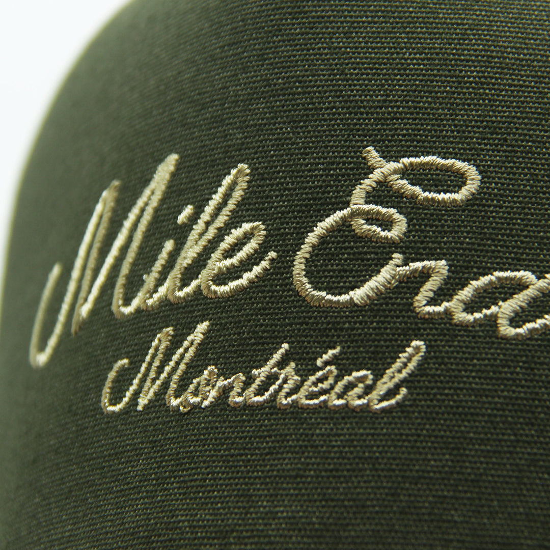Green cap with embroidered text 'Mile End Montreal' on a blurred background