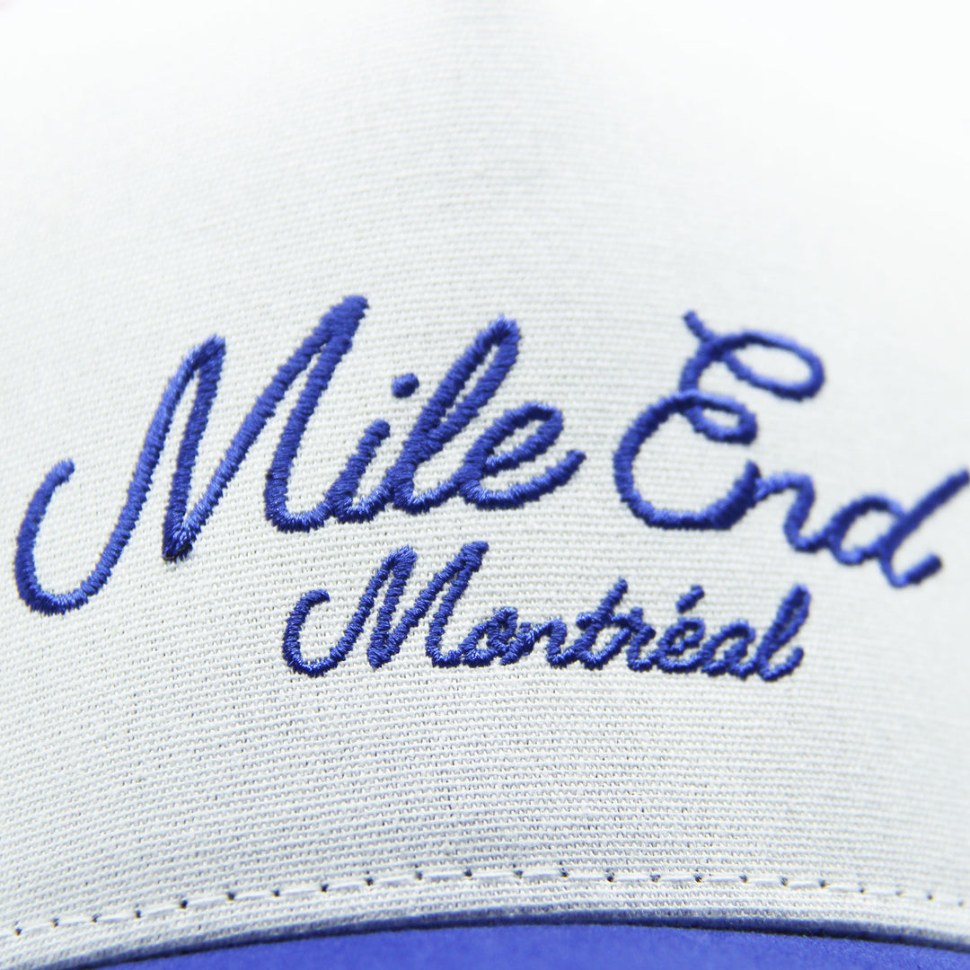 Close-up of a cap with 'Mile End Montreal' embroidered in blue on a white background