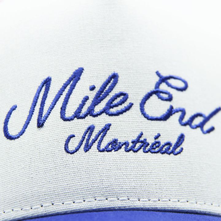 Close-up of a cap with 'Mile End Montreal' embroidered in blue on a white background