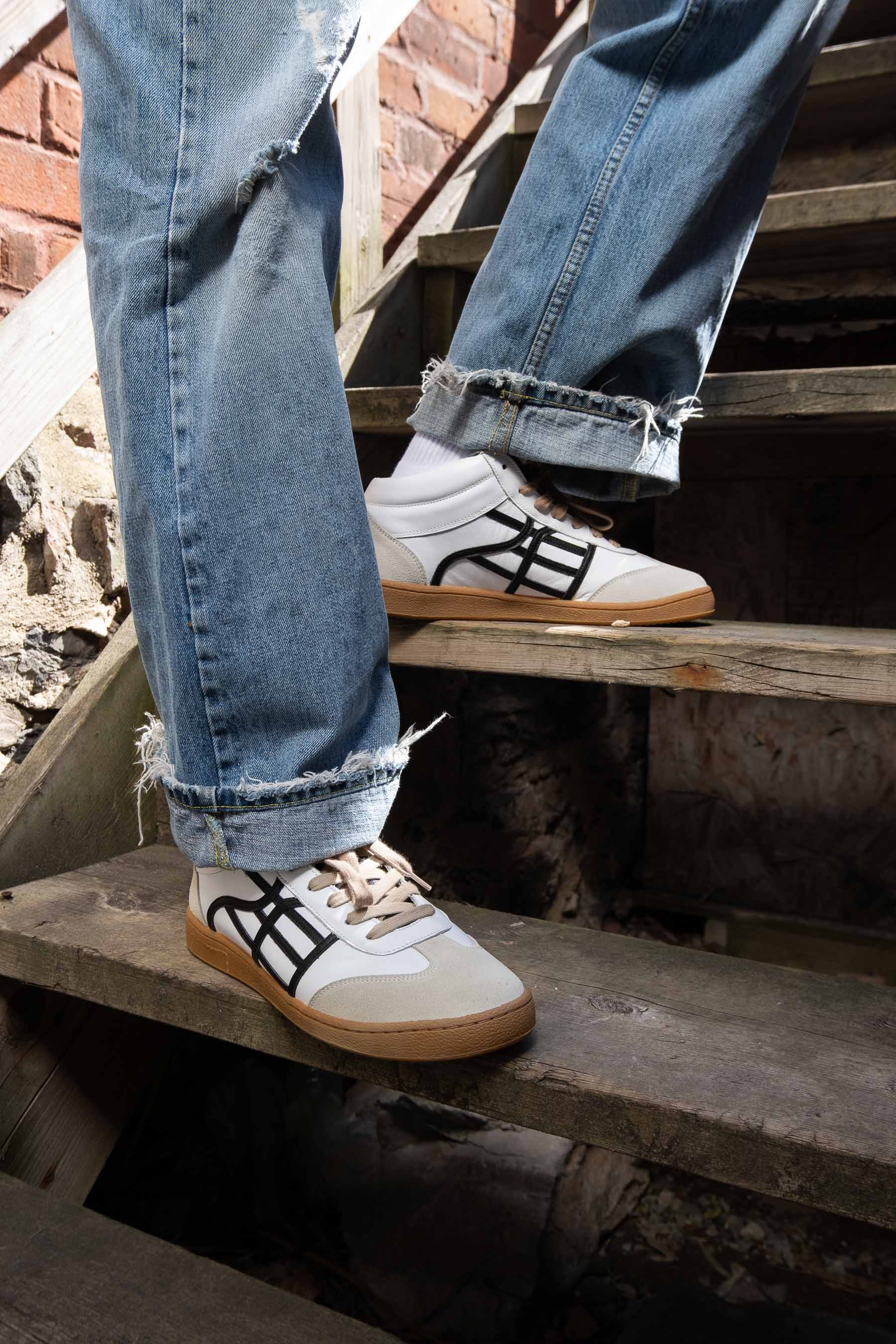 Person wearing blue jeans and white sneakers with black logo on a set of stairs.
