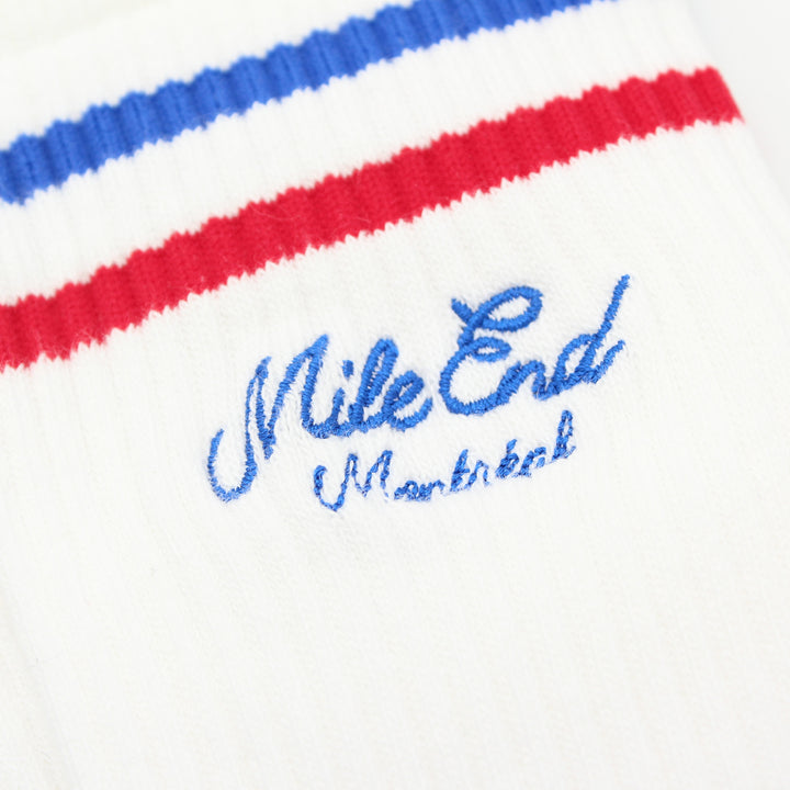 Close-up of a white sock with red and blue stripes and 'Mile End Montreal' embroidery.