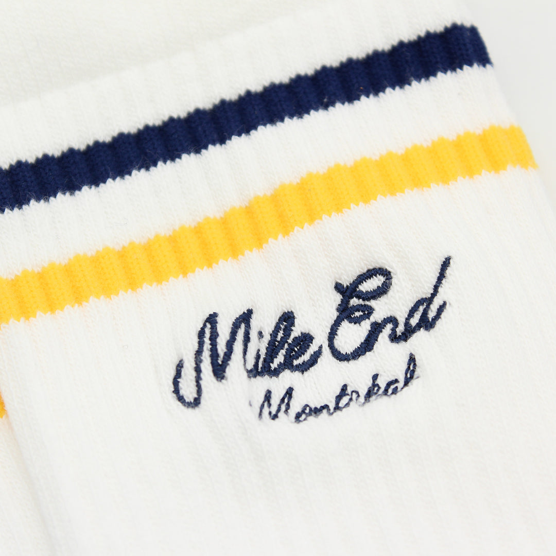Close-up of a white sock with blue and yellow stripes and 'Mile End Montreal' text.