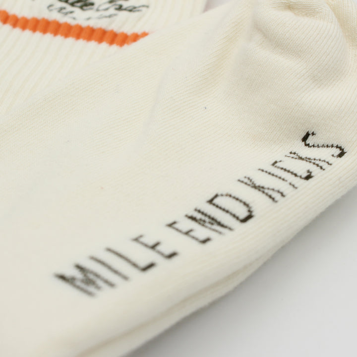 Close-up of a white sock with black text and orange trim on a light background