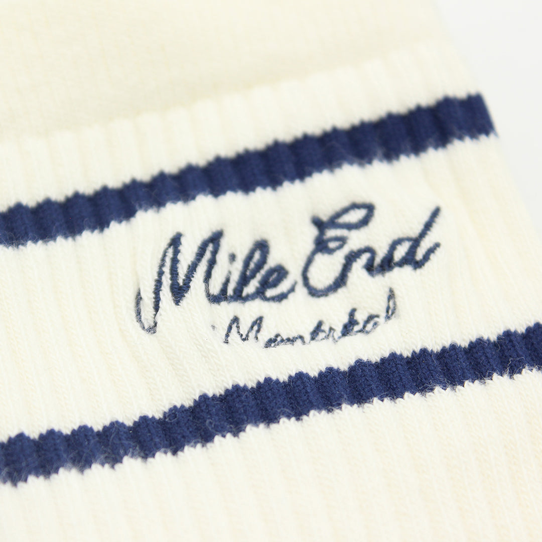 Close-up of white socks with blue stripes and 'Mile End Montreal' text.