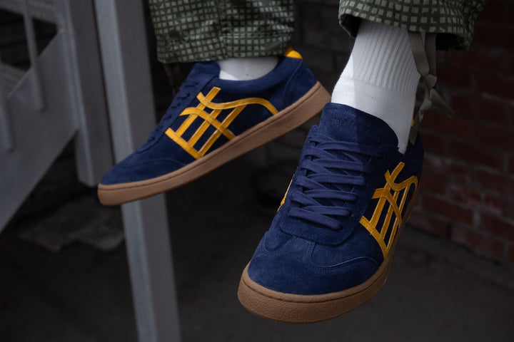 Blue sneakers with yellow accents worn by a person.