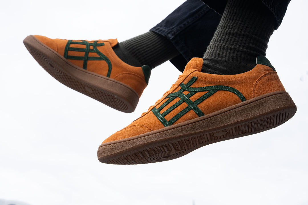 Orange sneakers with green accents worn by a person on a white background