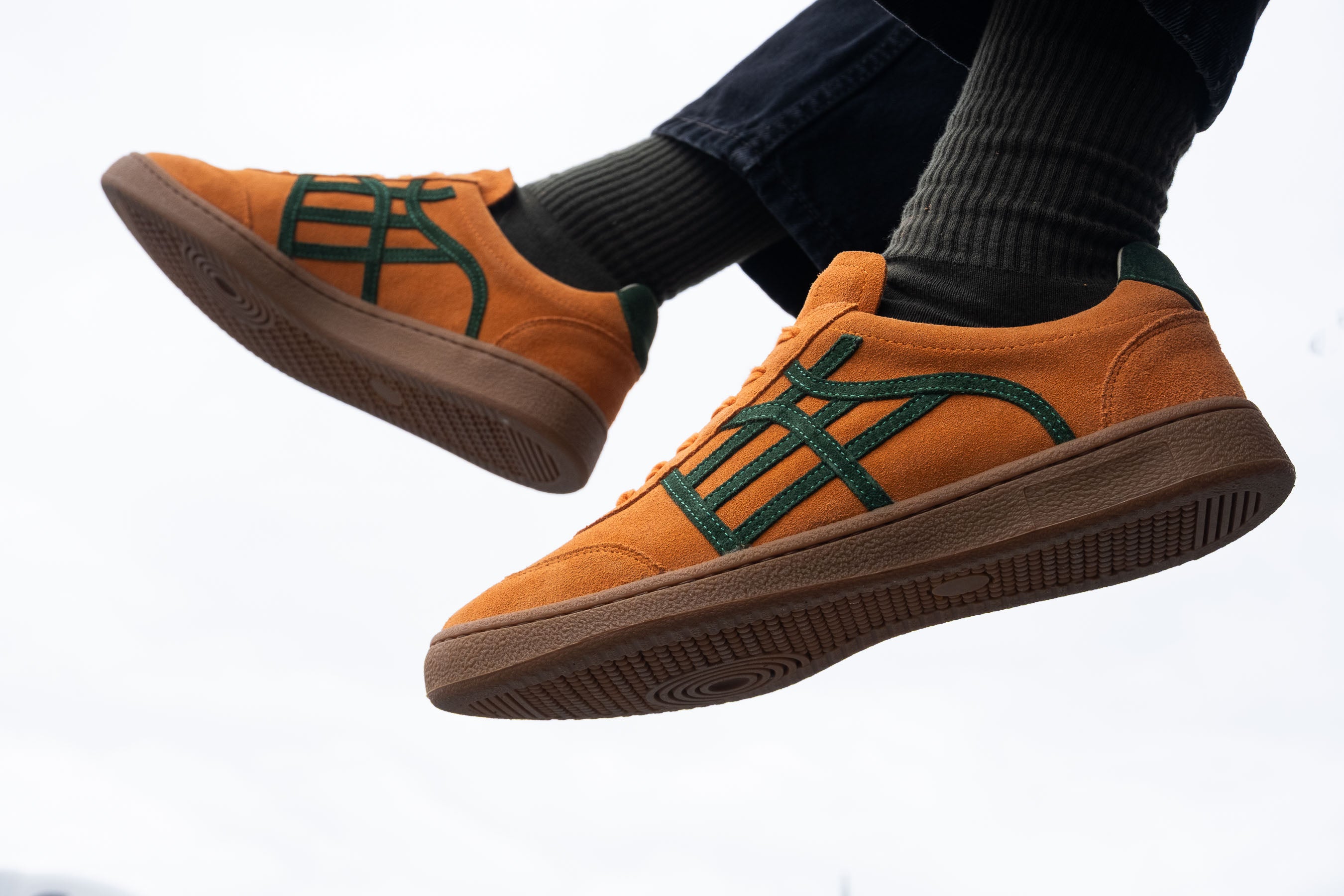Orange sneakers with green accents worn by a person on a white background