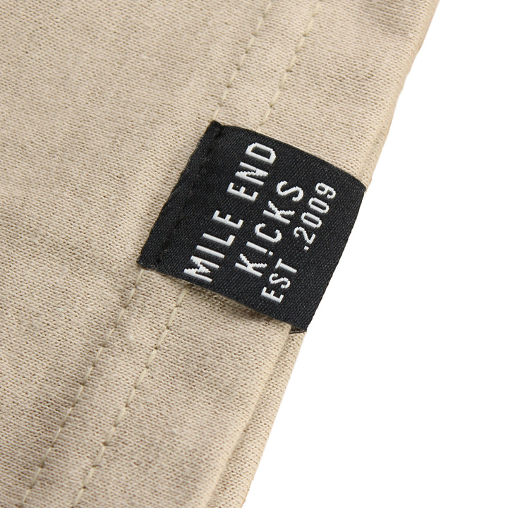Close-up of a beige fabric with a black label reading 'Mile End Kicks Est. 2009'.